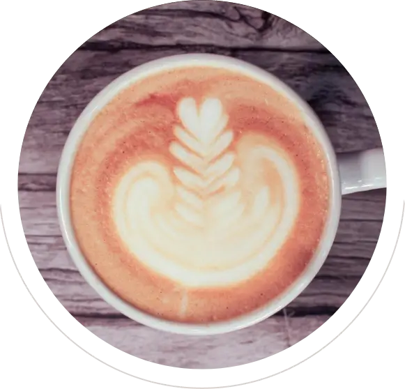 A cup of latte with intricate leaf latte art on top.
